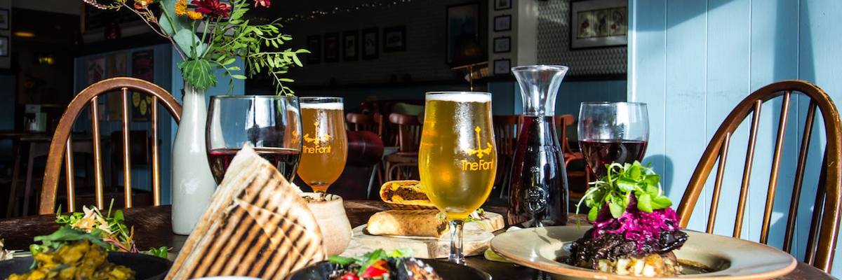 Sunlight falls on a table laden with beers, wine and colourful food at The Font Chorlton