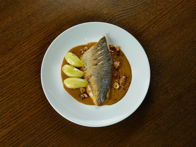 A dish of wild Liverpool Bay Sea Bass with laksa emulsion, Ratte potatoes, crispy chilli oil, sea herbs and crispy brown shrimp at Barnacle in Liverpool.