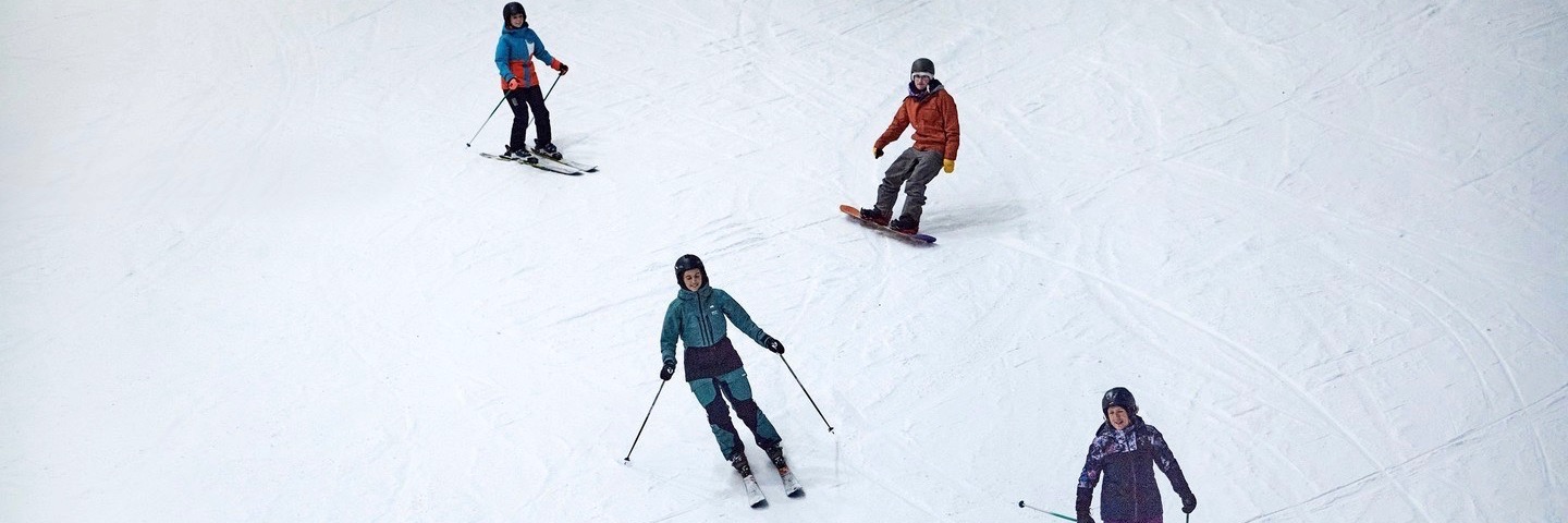 Four people skiing and snowboarding at Chill Factore - a real snow indoor ski slope in Trafford Park, Greater Manchester