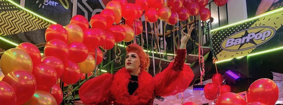 A drag queen stood by red balloons at Bar Pop