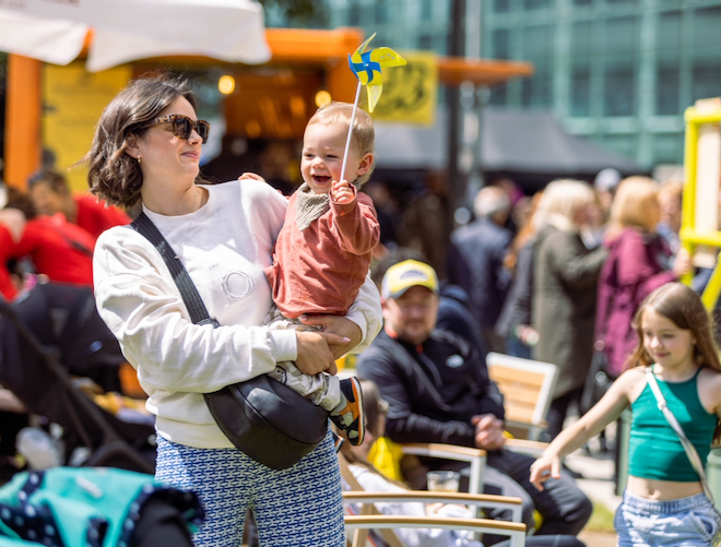 A mother with a baby who is holding a windmill toy at We Invented The Weekend festival in Salford.