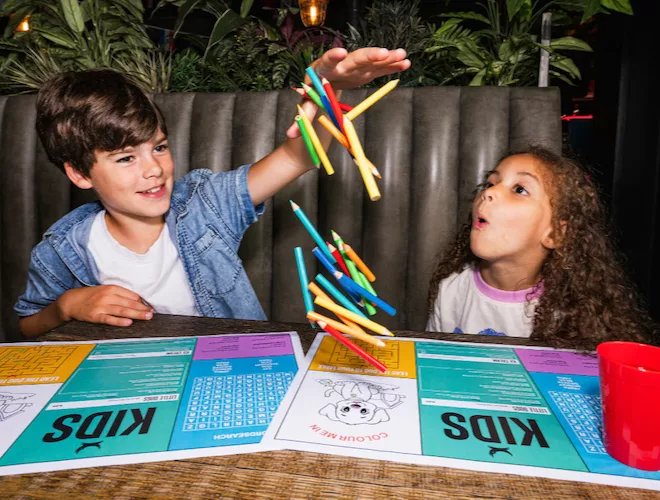 A boy dropping a handful of crayons over a menu at a BrewDog venue.
