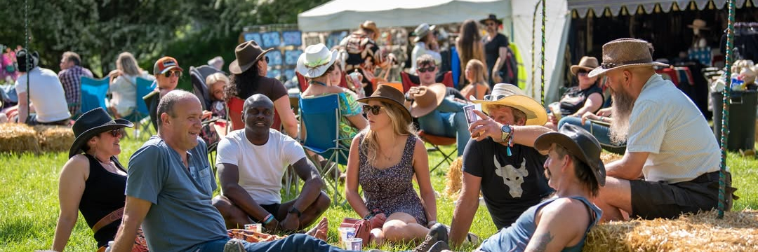 A group of country music fans sitting on the grass and hay bales at Buckle and Boots Festival.