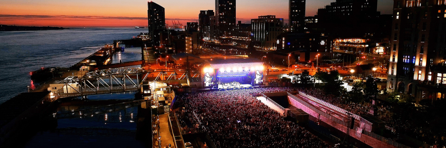 Aerial view of Liverpool waterfront at dusk with a crowd and stage for On The Waterfront festival.