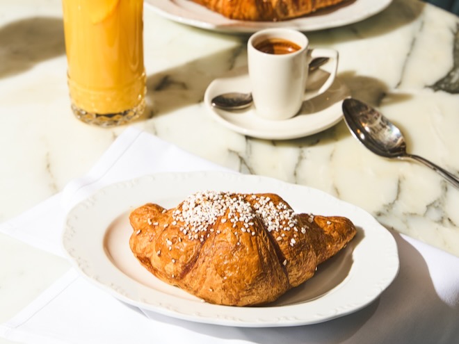A croissant, coffee and orange juice on a marble table at Cicchetti Manchester.