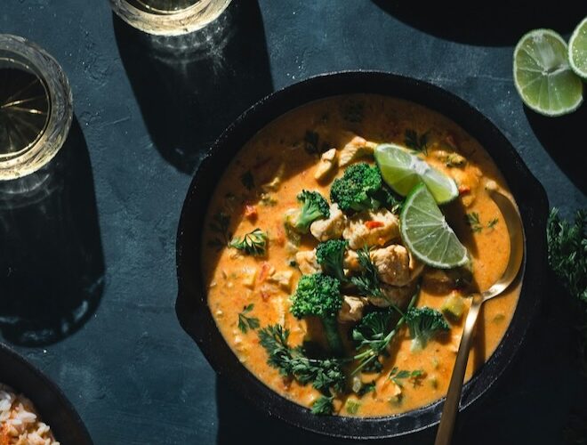 A black bowl of Thai red curry on a grey marble table.