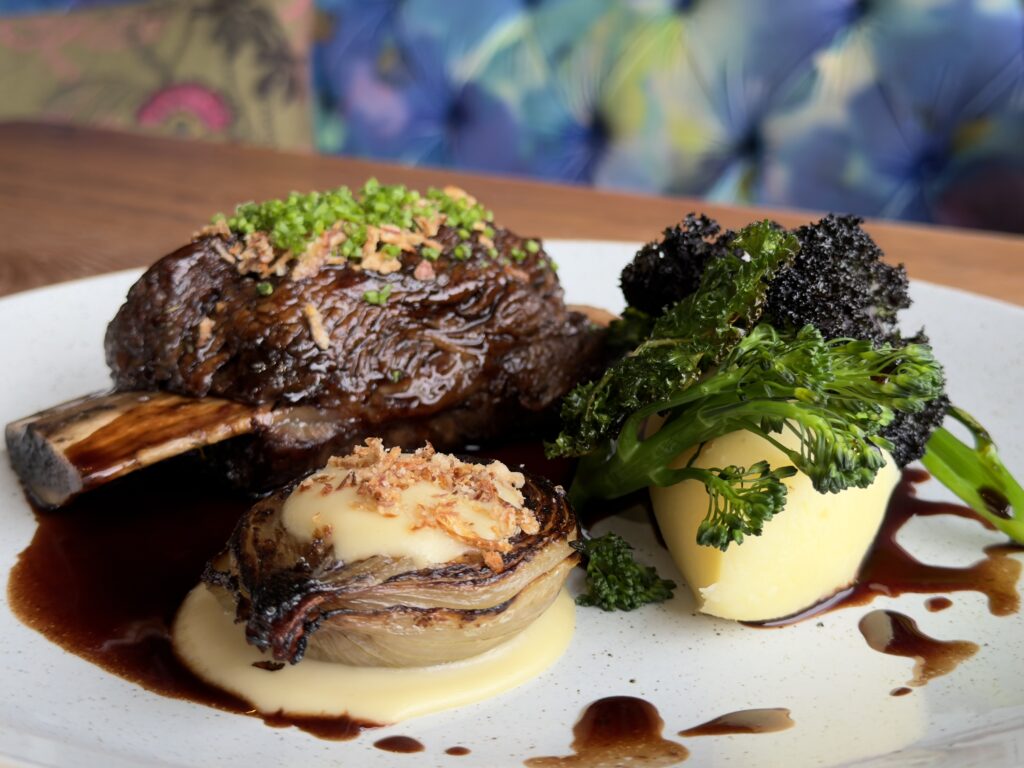 Lamb shank on the bone served with creamy mash, tender broccoli, roasted shallot with a homemade sauce and fresh seasonings, served at Riva Hale Restaurant.