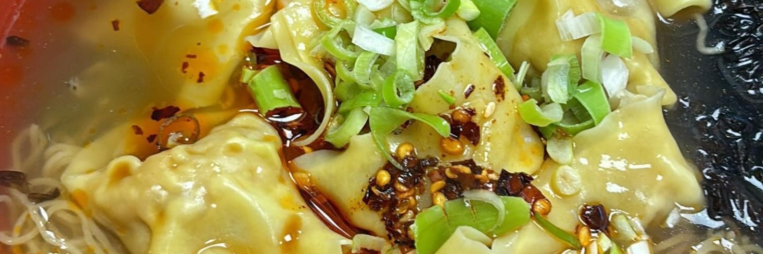 Wang's Dumplings topped with shredded spring onion and chilli sauce in a noodle broth