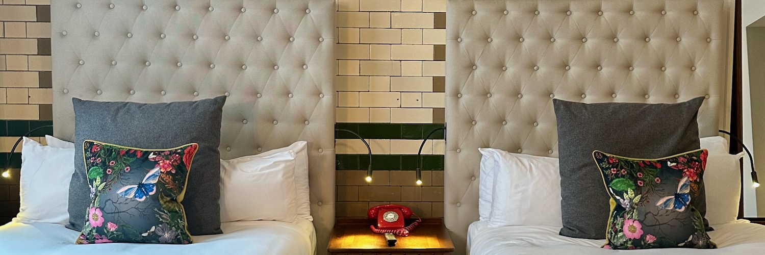 Two headboards with a red telephone and colourful cushions at The Kimpton Clocktower Hotel.
