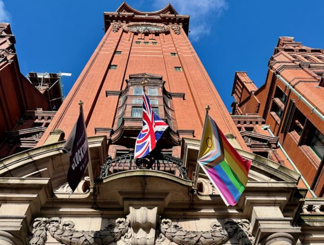 Looking up at the tower of the Kimpton Clocktower Hotel on a sunny day with flags flying over the door.