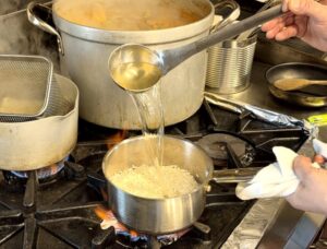 Chef adding a ladle of stock to a pan of rice