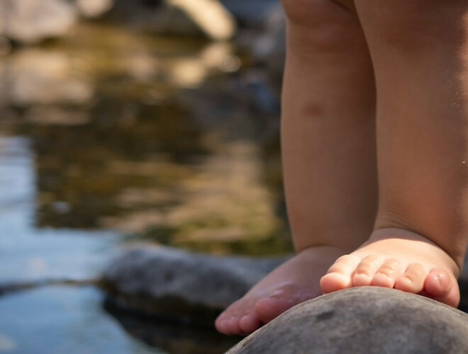 A toddler standing on a rock in a river.