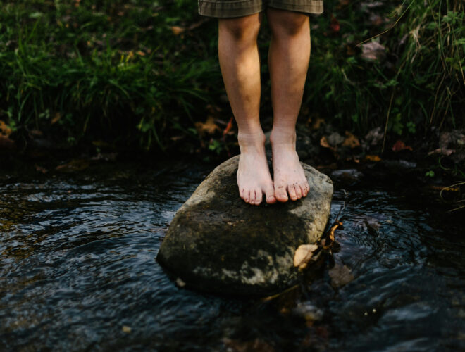 A child standing on a rock in a river.
