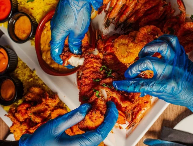 Three hands in blue vinyl gloves fighting over prawns at Shrimp & Co